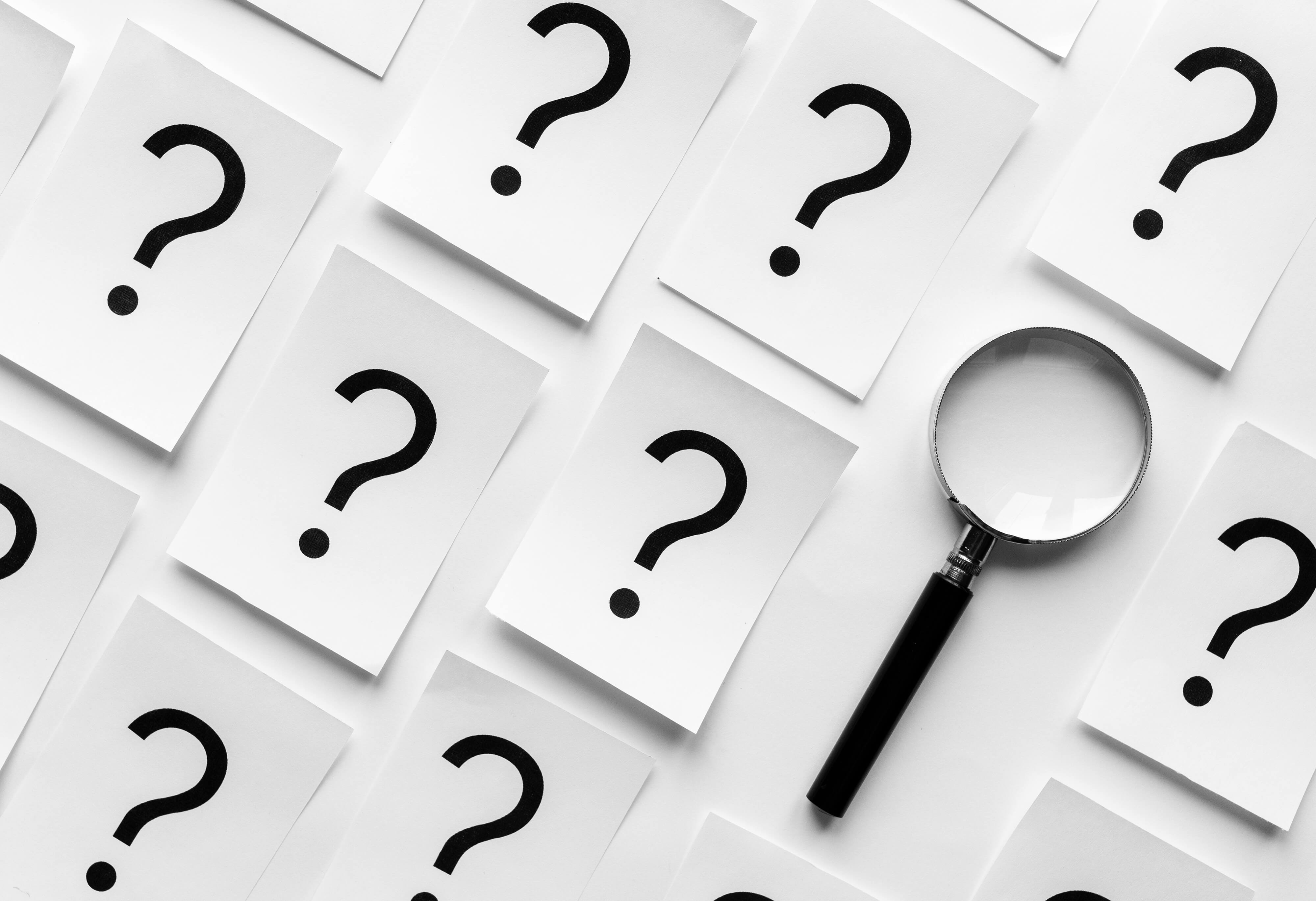 Cut Away Excessive Punctuation. Question marks on sheets of paper lay next to magnifying glass.