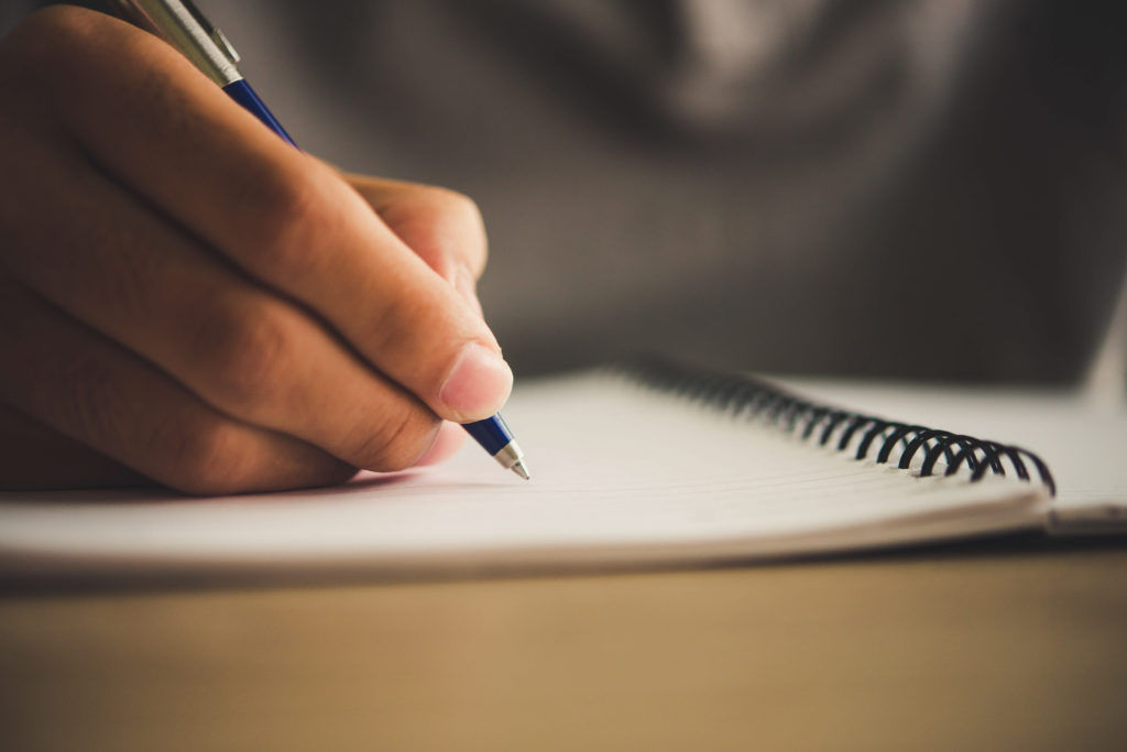What is a College Admissions Essay? Student holds pen over notebook, preparing to write.